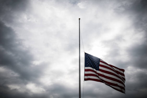 American Flag lowered to Half-Mast honoring a memorial American Flag lowered to Half-Mast honoring a memorial with a dramatic cloudy sunlight background flag at half staff stock pictures, royalty-free photos & images