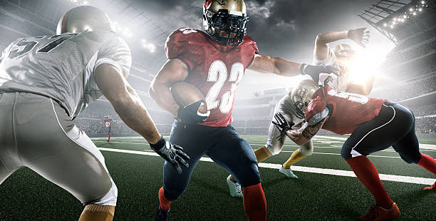 American football in action Action image of American football professional league players running with ball while matching with teammates and opposite players in outdoor floodlit stadium under sky with  sunlight. defending sport stock pictures, royalty-free photos & images