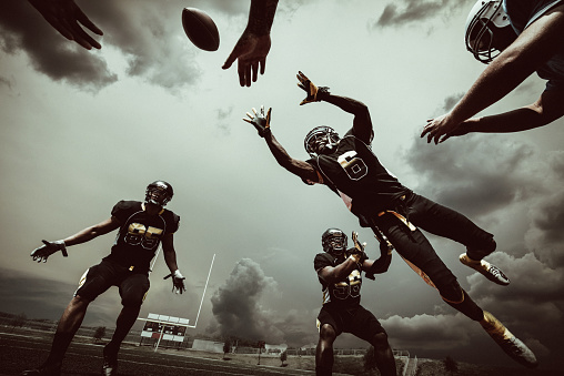 American Football Player jumping to catch the ball under dramatic sky.