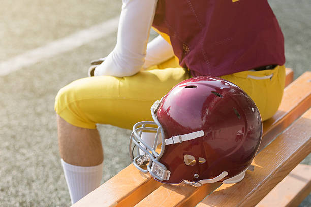 American football player sitting on bench next to sports helmet stock photo