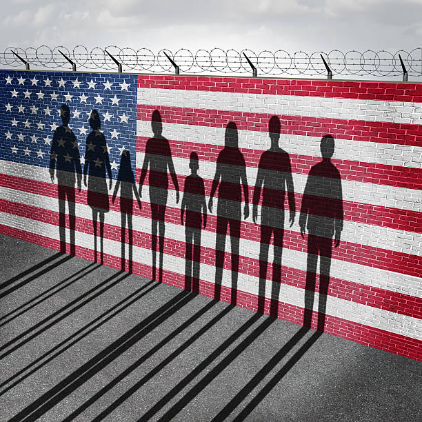American Immigration American immigration and United States refugee crisis concept as people on a border wall with a US flag as a social issue about refugees or illegal immigrants with the cast shadow of a group of migrating women men and children. border patrol stock pictures, royalty-free photos & images
