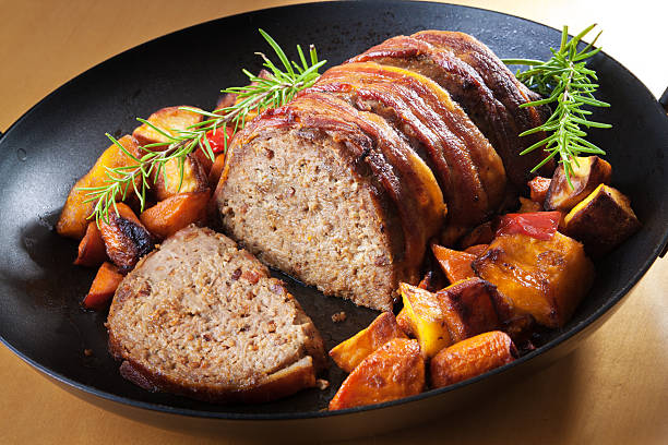 American Meatloaf with Roasted Potatoes Squash and Carrots Meatloaf, a favorite and popular American main dish, roasted with bacon covering and accompanied by roasted vegetable such as carrots, squash, and potatoes, garnished with sprigs of rosemary. Presented on a black iron roasting pan. meat loaf stock pictures, royalty-free photos & images