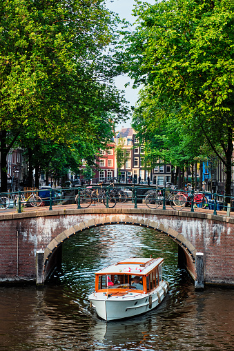 Amsterdam view - canal with boat passing under bridge and old houses. Amsterdam, Netherlands