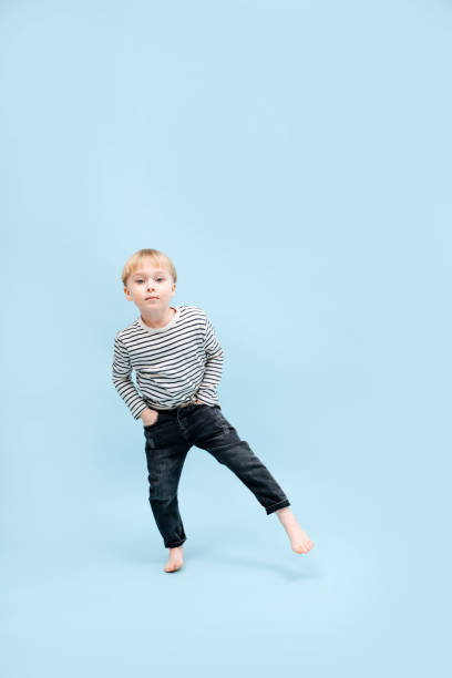 Amusing blond boy standing on one foot, shifting his weight. Over blue stock photo