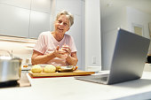 istock An 80-year-old senior citizen takes part in cooking classes online and uses her laptop or Macbook to cook in her own modern design kitchen 1296102044