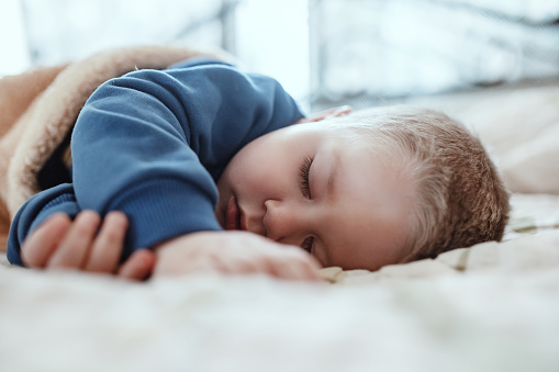 A close-up portrait of a cute little boy in blue pajamas sleeping peacefully on the bed