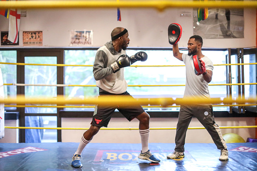 An Adult African male sparring with his boxing coach in the ring to warm up in a boxing gym in Cape Town, South Africa.