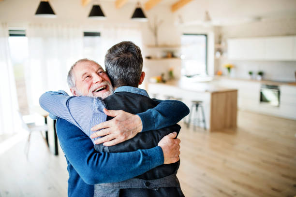 un figlio hipster adulto e un padre anziano al chiuso a casa, abbracciando. - abbracciare una persona foto e immagini stock