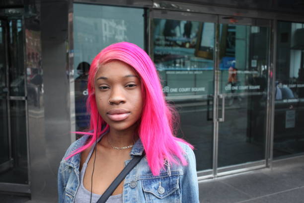 An African American woman with pink hair New York, NY USA - An Africna American woman standing in front of some glass doors looking into the camera. pink hair stock pictures, royalty-free photos & images
