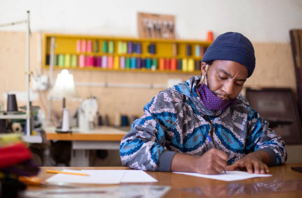 An African man sketching a design in his fashion design studio in Kayamandi South Africa. African fashion designers at work in their studio in Kayamandi informal settlement near Stellenbosch South Africa. textile industry photos stock pictures, royalty-free photos & images