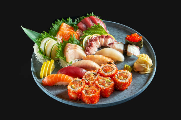 An appetizing sushi set consisting of various nigiri. sashimi and uramaki with salmon, avocado and tobiko caviar. Japanese traditional cuisine. Food delivery. Isolated on black stock photo