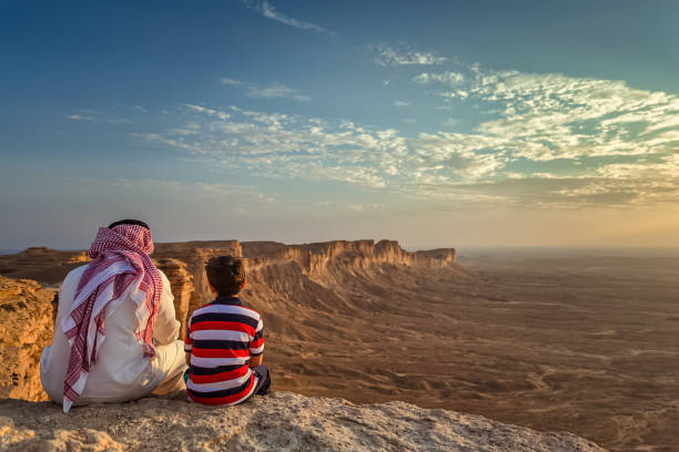 An arab man and his son sitting in Edge of the world, a natural landmark and popular tourist destination near Riyadh -Saudi Arabia.08-Nov-2019. Selective focus and background blurred. stock photo