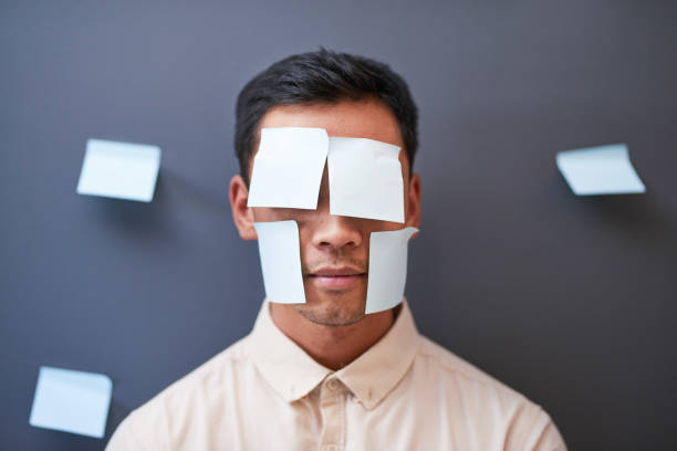 An Asian businessman stands with sticky notes on his face looking tired at work stock photo