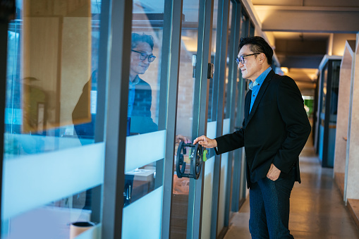 Side view of an Asian businessman standing at doorway opening door in office. Return to work concept.