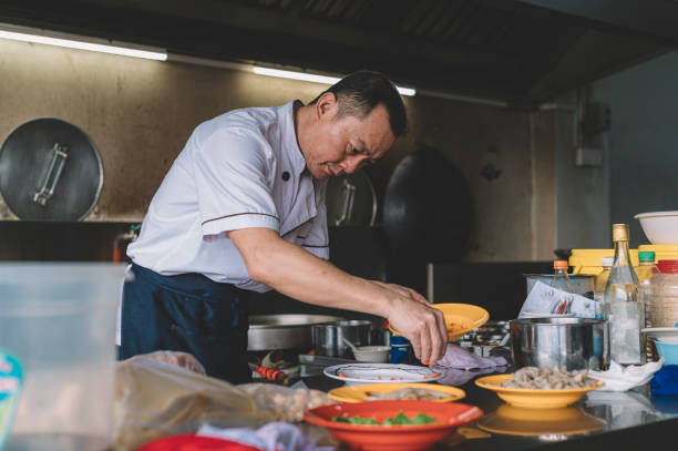 ein asiatischer chinesischer chef kocht in der kommerziellen küche und bereitet essen für seinen kunden vor - asiatischer koch stock-fotos und bilder