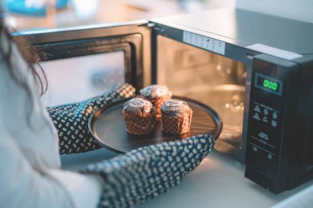 an asian chinese female putting cakes on a plate to microwave to heat up wearing kitchen glove an asian chinese female putting cakes on a plate to microwave to heat up wearing kitchen glove microwave stock pictures, royalty-free photos & images