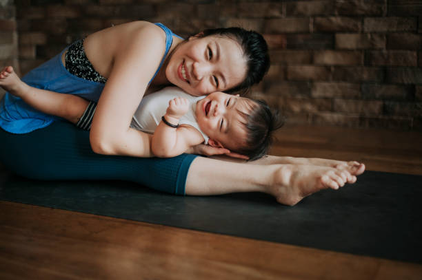 an asian chinese female yoga instructor workout together with her 9 month old baby boy son in the living room with brick wall on yoga met  asian yoga pants stock pictures, royalty-free photos & images
