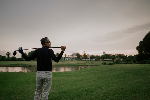 an asian chinese senior man golfer carrying his golf club on his shoulder and looking at the view in golf course
