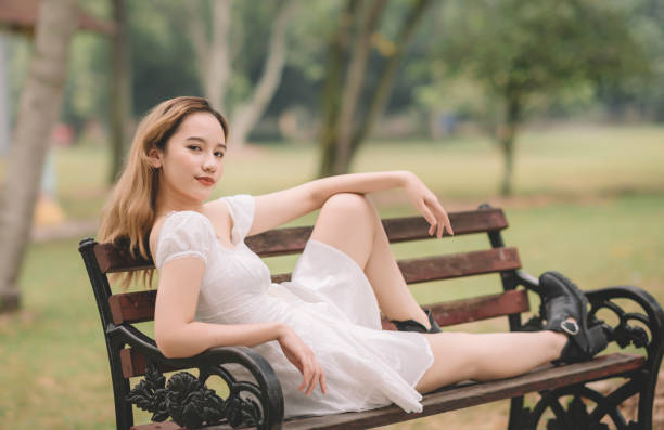 an asian female teenager girl sitting on the wooden bench at public park an asian female teenager girl sitting on the wooden bench at public park girls in very short dresses stock pictures, royalty-free photos & images