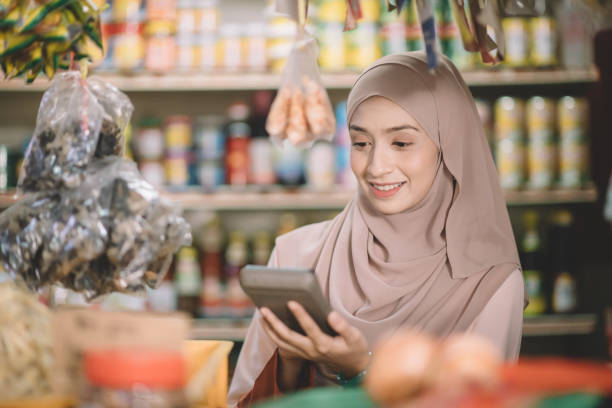 an asian malay groceries shop female owner with hijab calculating the price of the item for her customer an asian malay groceries shop female owner with hijab calculating the price of the item for her customer business Malaysia stock pictures, royalty-free photos & images