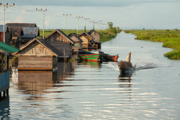 An asian Man is down the lake and rows of houses on stilts using a motorboat stock photo