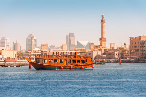 An authentic wooden cruise ship cruises and transports tourists along the Dubai Creek Canal with skyscrapers and minarets of mosques in the background. Travel and sightseeing An authentic wooden cruise ship cruises and transports tourists along the Dubai Creek Canal with skyscrapers and minarets of mosques in the background. Travel and sightseeing dhow stock pictures, royalty-free photos & images