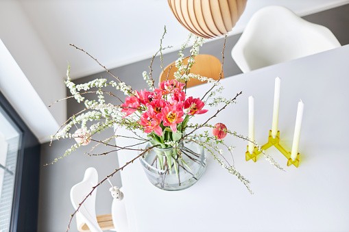 A modern Easter bouquet with tulips and twigs stands in a bright environment on a white table in a glass vase