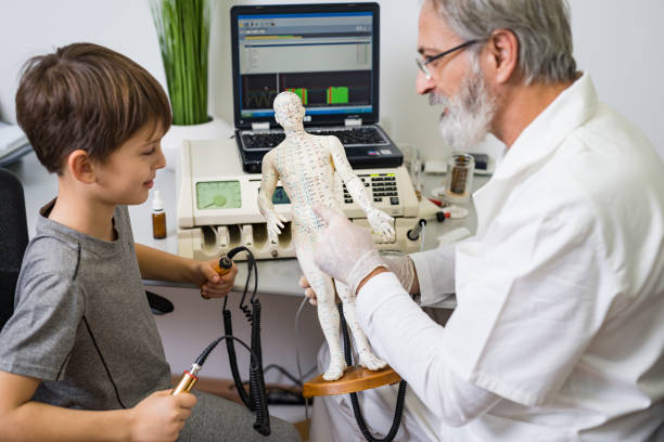 An elderly doctor - bioresonance therapist with gray hair and a beard works bioresonance therapy on a sick child with a bioresonance device stock photo