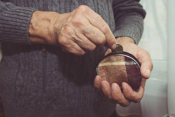 An elderly man puts a coin in an empty wallet. Poverty in retirement concept. Special toning stock photo