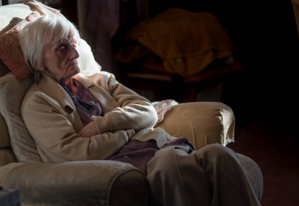 An elderly woman feeling isolated,alone and cold at her home during the winter months. A ninety year old lady is covered in an insulating blanket to try and stay warm and is unable to leave her house unaided as she is registered blind and frail. solitude stock pictures, royalty-free photos & images