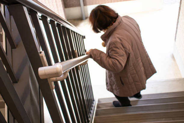 An elderly woman holding a railing and going down the stairs. An elderly woman holding a railing and going down the stairs. bannister stock pictures, royalty-free photos & images