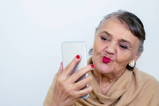 An elderly woman with a phone. Old lady hipster takes a selfie. An elderly woman masters the technique, the phone. Elderly, technology concept. Trendy hipster woman having fun with smartphone. stock photo