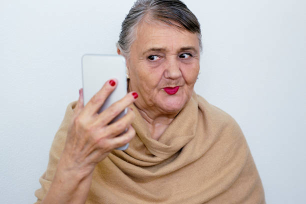 An elderly woman with a phone. Old lady hipster takes a selfie. An elderly woman masters the technique, the phone. Elderly, technology concept. Trendy hipster woman having fun with smartphone. stock photo