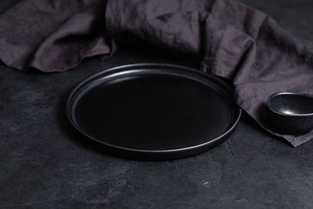 An empty stylish plate and gravy boat black on a black table background stock photo