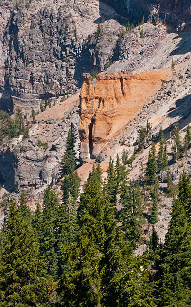 Pumice Castle Rock Formation An eruption occurred 70,000 years ago and formed the pink, buff and orange Pumice Castle formation on what is now the east side of Crater Lake. Subsequently it was buried by the Redcloud Cliff flow and then exposed when Mount Mazama erupted and its caldera collapsed. Rain and wind have since finished the job of carving the pumice into its hoodoo shaped formations. Pumice Castle sits about 1,300 feet above the surface of Crater Lake in Crater Lake National Park, Oregon, USA. jeff goulden crater lake national park stock pictures, royalty-free photos & images
