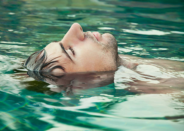 An image of a man with his eyes closed floating in water Portrait of a young man relaxing in the swimming pool floating on water stock pictures, royalty-free photos & images