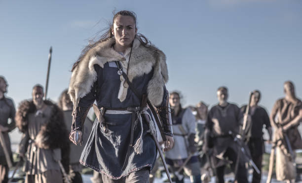 un individual femenino viking haciéndose pasar frente a un grupo de guerreros estaba parado en las olas en la orilla - warriors fotografías e imágenes de stock