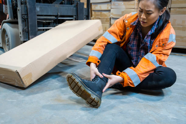 An industrial warehouse workplace safety topic.  A female employee injured by tripping over forklift forks. stock photo