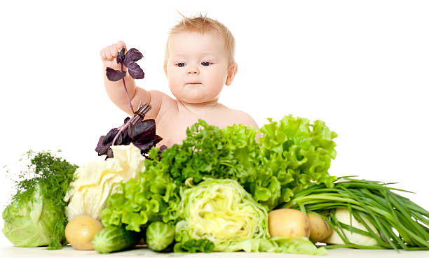 An infant playing with different types of vegetables stock photo