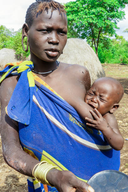 An infant with its mother in the  blue and yellow clothes in the local Mursi tribe village stock photo