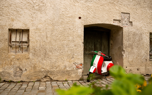 25 May 2019, Rome, Italy - Vintage motorbike in italian flag colors parked near old rustic wall. Inspiring atmospheric spirit of Italy. Large textured foreground on left side of wall.