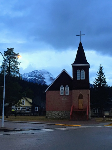Jasper, Canada - November 12th, 2016: An old small church nestled at the base of the Rocky Mountains on a dark stormy night in Jasper, Alberta, Canada