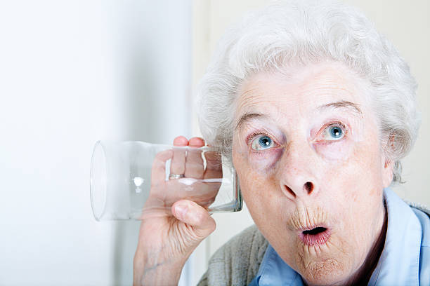 An old woman looking shocked with a glass on her ear stock photo