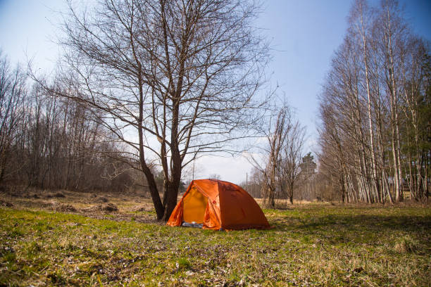 An orange tent built on the bank of the river. Hiking camp in the...