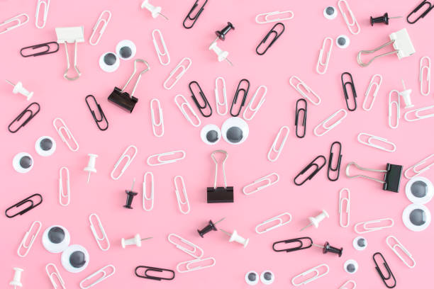 An unusual pink background with a pattern of stationery chaotically scattered. Smiley from puppet eyes and clips in the center. stock photo