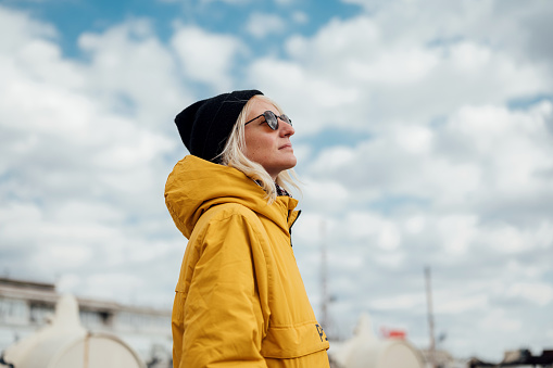 Low angle view of a young urban woman in yellow jacket and black hat with hands in her pocket looking up