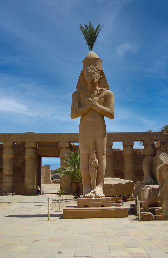Ancient statues of Pharaoh Ramses II and his daughter Meritamon in the temple of Karnak, Luxor, Egypt. No people. Blue sky.