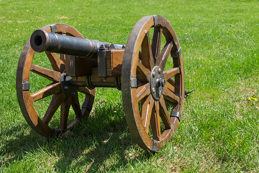 Ancient war cannon with wooden wheals on green grass|military
