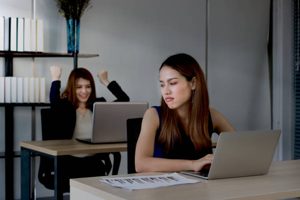 Angry envious Asian business woman looking successful competitor colleague in office. Low key toned image Angry envious Asian business woman looking successful competitor colleague in office. Low key toned image envy stock pictures, royalty-free photos & images