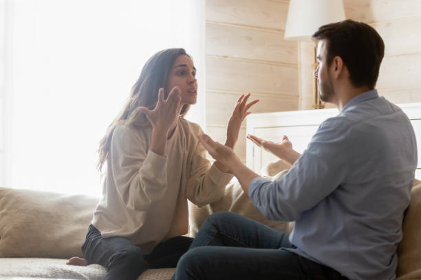 Angry millennial couple have troubles dispute at home Angry young couple sit on couch in living room having family fight or quarrel suffer from misunderstanding, millennial husband and wife dispute involved in argument, relationships problems concept fighting stock pictures, royalty-free photos & images